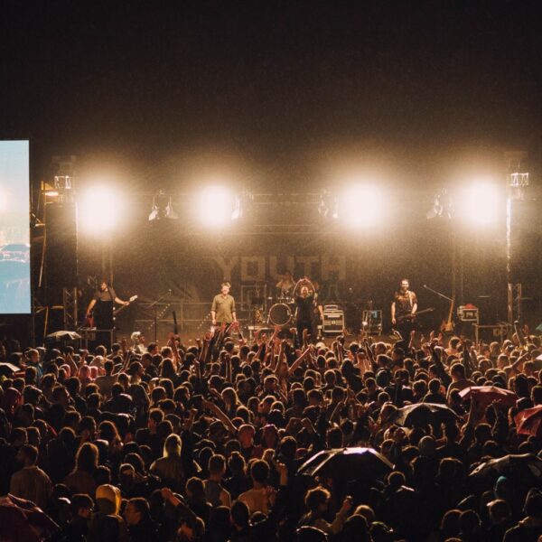 Menschenmenge steht abends vor einer hell erleuchteten Konzertbühne.