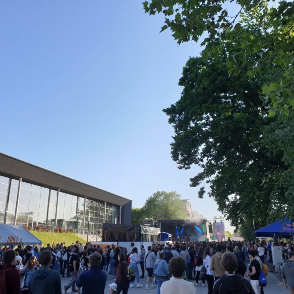 Bild vom Audimax. Davor stehen Menschen an Zelten und Pavillons.