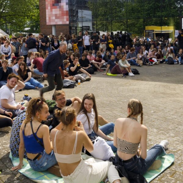 Festivalbesucher sitzen tagsüber auf dem Boden und unterhalten sich.