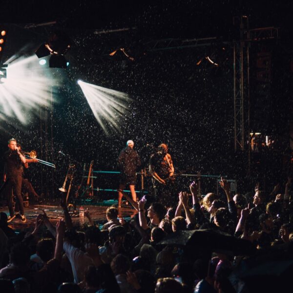 Band spielt auf einer Bühne mit Scheinwerfern, Publikum jubelt davor.