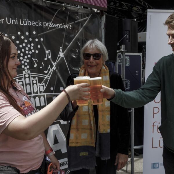 Zwei Frauen und ein Mann stoßen mit Bierbechern auf einem Festival an.