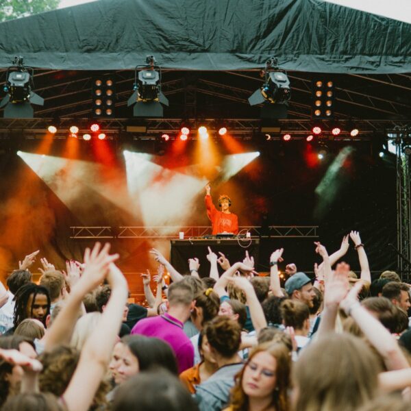 Menschen mit erhobenen Händen vor einer Bühne mit roter und gelber Beleuchtung.