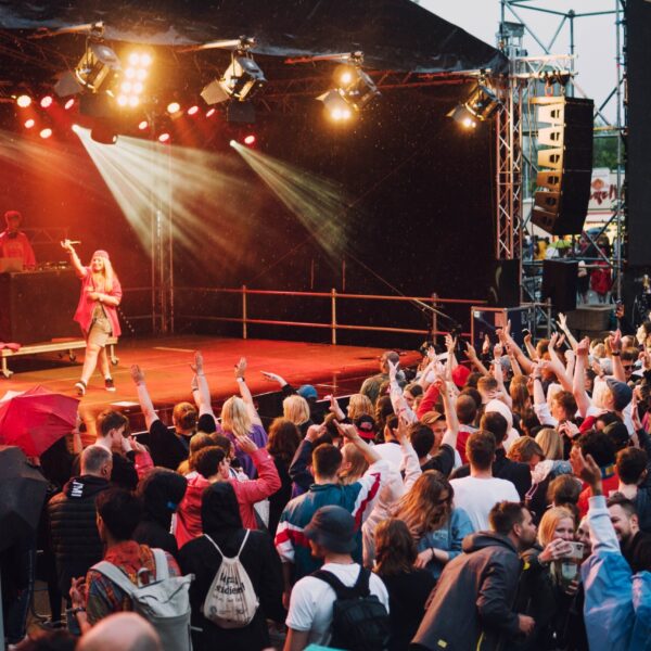 Menschen mit erhobenen Händen vor einer Bühne mit roter und gelber Beleuchtung.