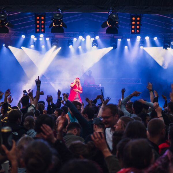 Konzertbühne mit blauer Beleuchtung, Musiker auf der Bühne und jubelndes Publikum.