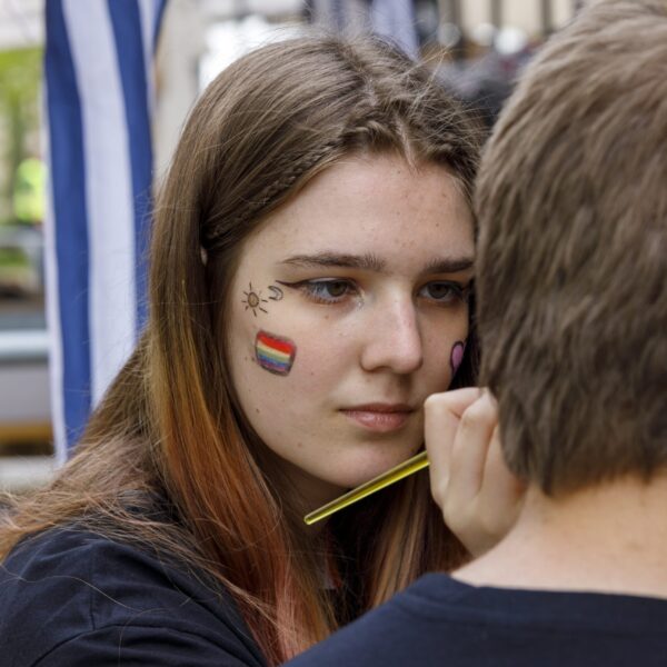 Frau mit aufgemaltem Deutschland-Flaggenmotiv im Gesicht, während sie jemanden schminkt.