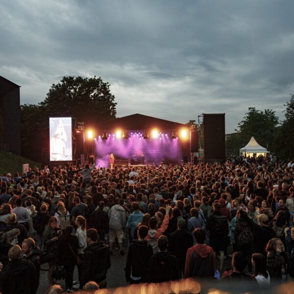 Menschenmenge bei einem Open-Air-Konzert am Abend mit Bühne und Beleuchtung.