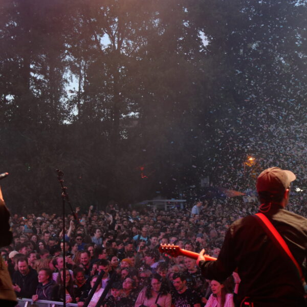 Menschenmenge von der Bühne aus Fotografiert. 2 Personen stehen im Vordergrund auf der Bühne. Die rechte spielt Gitarre und die linke singt.