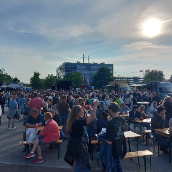 an Biertischen sitzen viele Menschen, essen und hören der Musik zu