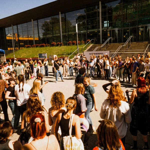 Auf der Fläche vor der Main Stage steht eine Menge an Menschen in einem Kreis. In der Mitte vom Kreis ist ein freier Platz.